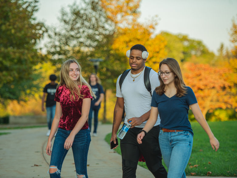 Two female and one male student walk across campus.